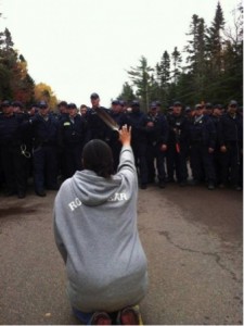 In 2013, Mi’kmaq mother Amanada Polchies made international news when kneeling in front of a line of police, raising a feather in her hand at an anti-fracking barricade in New Brunswick Canada. 